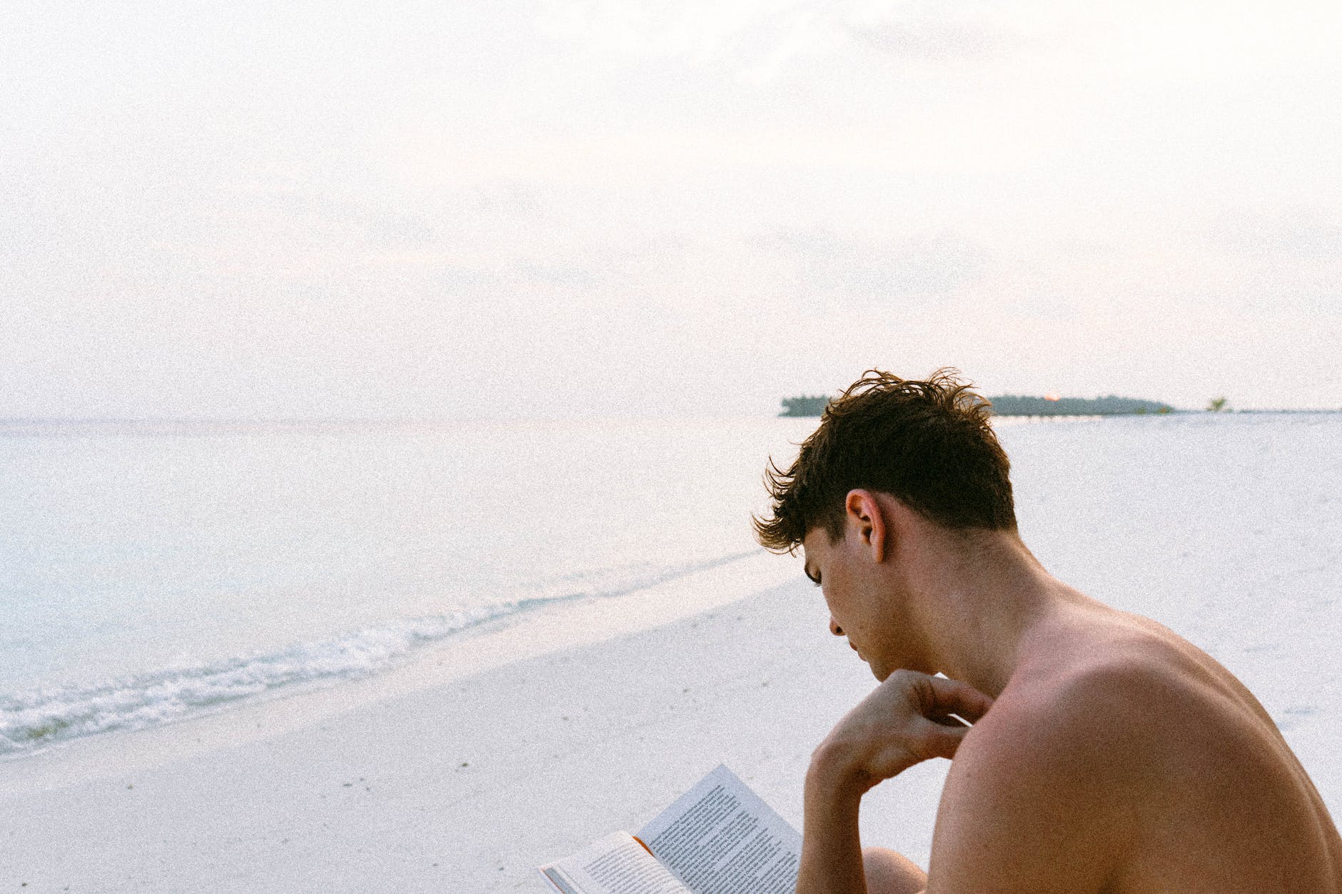 topless man reading book while seating at beach